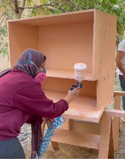 A woman is painting a wooden box. Description generated by AI